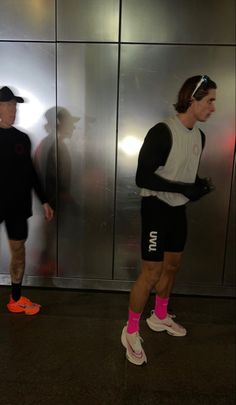 two men standing next to each other in front of a metal wall with mirrored doors