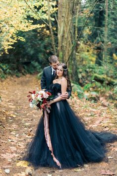 a bride and groom standing in the woods