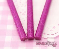 three purple glittered candles sitting on top of a pink tablecloth with white doily