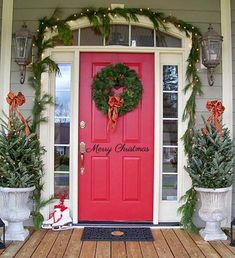 a red front door with christmas wreaths on it and two potted plants in front