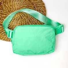 Pictured is a rectangle fanny pack with a top zipper with tassel in turquoise. This bag also includes a turquoise strap and turquoise accents. This bag is pictured on a white and brown patterned background. Green Crossbody Chest Bag For On-the-go, Green Belt Bag With Pockets For On-the-go, Green Chest Bag With Adjustable Strap For Everyday, Everyday Green Chest Bag With Adjustable Strap, Versatile Green Chest Bag With Adjustable Strap, Trendy Green Chest Bag For Everyday Use, Trendy Green Belt Bag With Zipper Closure, Trendy Green Everyday Chest Bag, Green Chest Bag With Zipper For Everyday Use