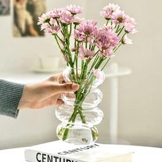 a person is holding flowers in a vase on top of a book that sits on a table