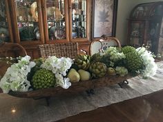 a wooden wheelbarrow filled with flowers and fruit on top of a dining room table