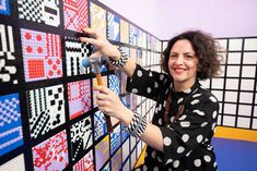 a woman is working on an art project in front of a wall covered with squares and dots