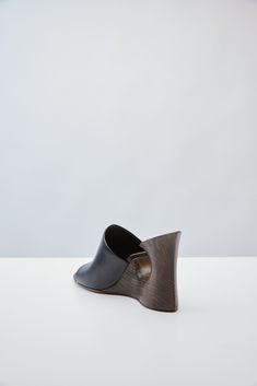 These mules from Alaïa's Pre-Fall 2024 collection are a testament to the house's craftsmanship with their hand-sculpted wooden base and their black calfskin upper. Designer Leather Clogs With Wooden Heel, Luxury Leather Clogs With Wooden Heel, Modern Leather Clogs With Sculpted Heel, Modern Leather Mules With Wooden Heel, Leather Mules With Rubber Heel Cap For Formal Wear, Elegant Black Clogs With Leather Sole, Formal Leather Mules With Rubber Heel Cap, Modern Black Clogs With Sculpted Heel, Designer Black Mules With Sculpted Heel