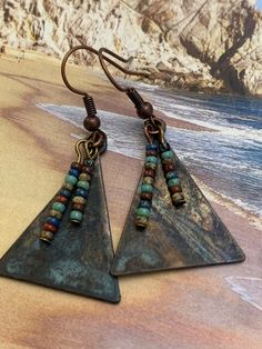 Copper and Glass Earrings. Triangular copper metal that has patina finish. Tiny earth multi-colored Czech glass beads adorn and dangle on the front. Unique handcrafted earrings. Sure to be your favorite pair! Highest Quality Craftmanship. Nickel-free Bronze Artsy Earrings, Brown Artisan Metal Earrings, Artisan Brown Metal Earrings, Artisan Metal Earrings In Rust Color, Artisan Metal Rust Earrings, Bohemian Triangle Earrings With Ear Wire, Artsy Copper Jewelry With Matching Earrings, Artsy Nickel-free Copper Earrings, Artisan Metal Beaded Earrings Nickel Free