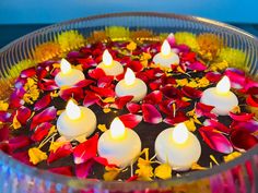 candles are floating in a bowl filled with water and red, yellow and white flowers