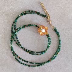 a green beaded necklace with a gold flower on the end and a chain attached to it