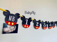 a baby's first birthday banner with mickey mouse ears and numbers hanging from the wall