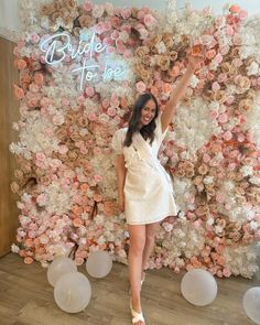 a woman standing in front of a flower wall with her arms up to the side