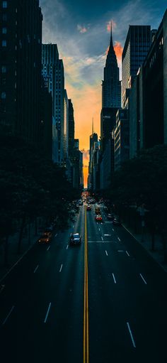 a city street with tall buildings and cars driving down the road at sunset or dawn