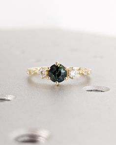 a green diamond ring sitting on top of a white surface with three diamonds around it