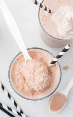 two glasses filled with ice cream on top of a white table next to spoons