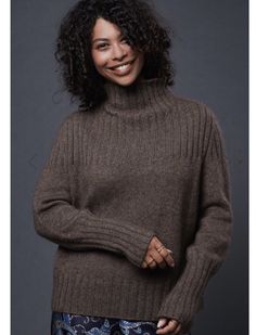 a smiling woman in a brown sweater and blue floral print pants stands with her hands on her hips