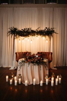 a table with candles and flowers on it in front of a white drape curtain