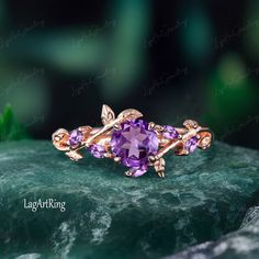 a gold ring with amethorate and leaves on it sitting on top of a green rock