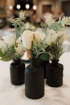 three black vases with white flowers in them