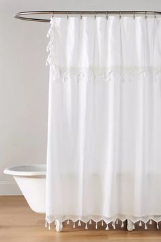 a white shower curtain with tassels hanging from it's side in front of a bathtub