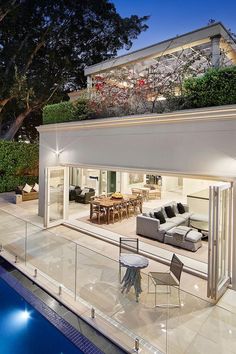 an outdoor living room and dining area with pool in the foreground at night time