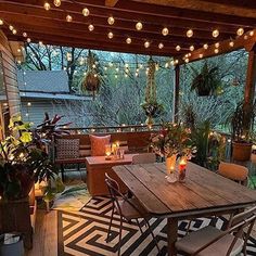 an outdoor dining area with lights strung from the ceiling and potted plants on the table