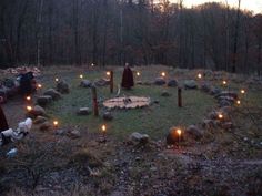 a person standing in the middle of a field surrounded by rocks and candles with trees in the background