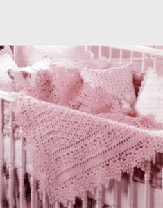 a pink crocheted baby blanket on top of a white crib next to pillows