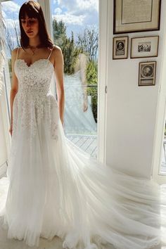 a woman standing in front of a window wearing a wedding dress