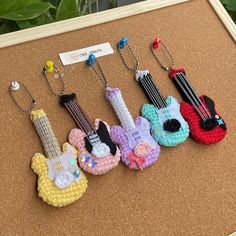 four miniature crocheted guitars are displayed on a cork board