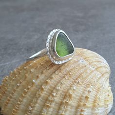 This sea glass ring would make a great gift for any beach lover, it is a really pretty piece with a contemporary look. The ring features a triangle shaped piece of English sea glass in a glowing mid green, almost olive. I have set the glass into a fine silver bezel on a sterling silver base with a cute dotty textured rim. The seaglass setting sits on a narrow sterling ring band made from round profile wire. This triangle stone ring is a bit of a statement piece but not too large for everyday wea Minimalist Beach Ring Jewelry, Minimalist Beach Jewelry Ring, Silver Sea Glass Ring For Beach, Green Stackable Jewelry For The Beach, Beach-ready Green Stackable Jewelry, Handmade Sea Glass Ring Jewelry, Handmade Adjustable Sea Glass Rings, Handmade Green Rings With Recycled Glass, Minimalist Sea Glass Jewelry For Beach