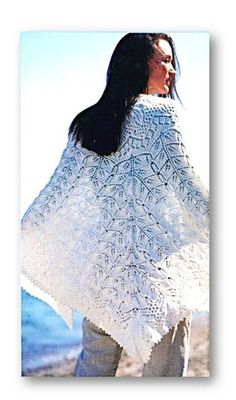 a woman wearing a white shawl standing next to the ocean