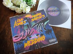 two vinyl records sitting on top of a wooden table next to flowers and a vase with white roses