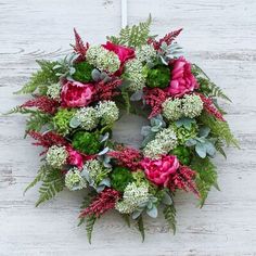 a wreath with flowers and greenery hanging on a white wooden wall, ready to be used as a decoration