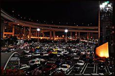 a large parking lot filled with lots of cars at night in front of an overpass