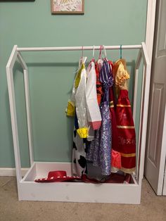 a white coat rack with several colorful scarves hanging from it's hooks in front of a blue wall