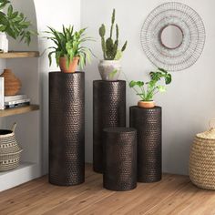 three black vases with plants in them on a wooden floor next to a wall