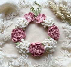 a crocheted wreath with pink and white flowers on it sitting on a lace doily