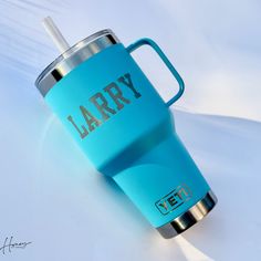 a teal colored travel mug with the word lary printed on it sitting on a white surface