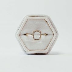 a white and gold ring sitting on top of a white box with a diamond in the middle