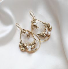 These handcrafted antique gold wedding earrings showcase a boho-inspired floral design, featuring delicate leaves and freshwater pearls. Expertly made to order, these hoop earrings add a touch of elegance and uniqueness to any bridal look. - Handcrafted in my PA studio - Genuine Austrian golden shadow crystal rock fabric leaves - Freshwater pearls - Antique gold leaves  - Available in rose gold, yellow gold or rhodium (silver) - Earrings measure 2.5 inches x 1-5/8 inch - Handcrafted in the US. - Floral Wedding Necklace, Vintage Wedding Earrings, Statement Wedding Earrings, Bridal Jewelry Gold, Jewelry For Bride, Wedding Earrings Vintage, Fabric Leaves, Antique Gold Earrings, Statement Earrings Wedding