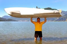 a man standing in the water holding up a boat on his head with mountains in the background