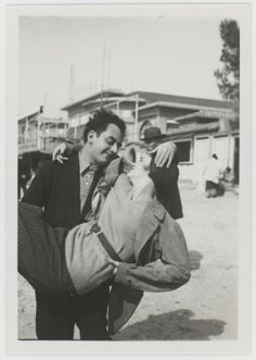 an old black and white photo of a man holding a cat in his arms while another man looks on