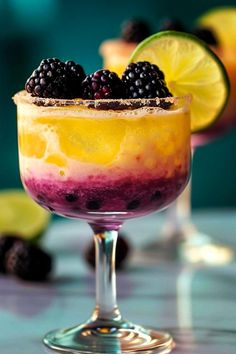 two glasses filled with food and garnished with blackberries, lemons and lime slices