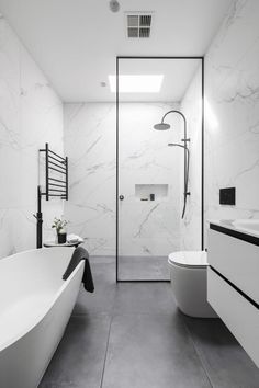 a modern bathroom with white marble walls and floor, along with a free standing tub