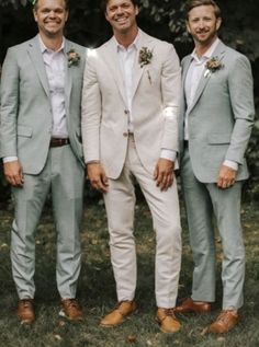 three men in suits and ties standing next to each other on the grass with trees in the background