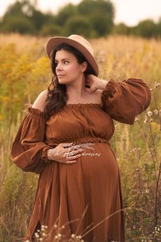 a pregnant woman wearing a brown dress and hat poses for a photo in a field