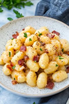 a white plate topped with macaroni and cheese covered in bacon next to a fork