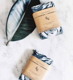 two bars of soap sitting on top of a marble counter next to a green leaf