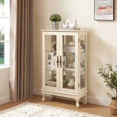 a white cabinet with glass doors in a living room next to a potted plant