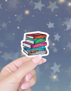 a hand holding up a sticker with books on it and stars in the background