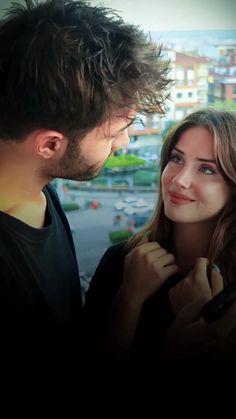 a man and woman standing next to each other looking at each other's eyes